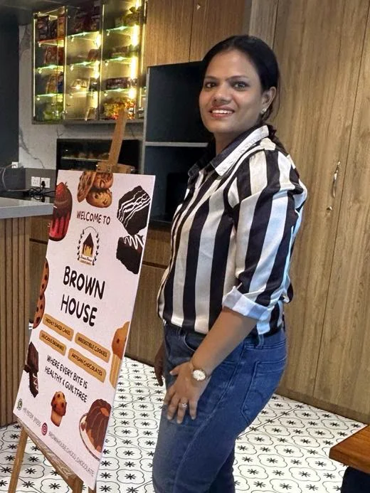 Neha Bansal, founder of Brown House, standing beside the Brown House standee at an office centre