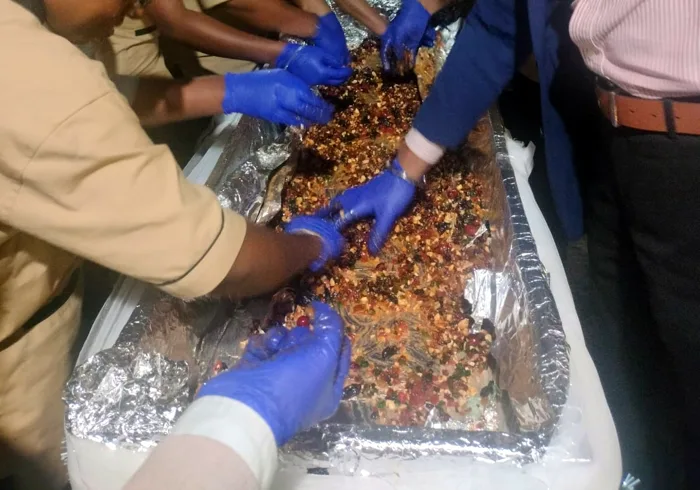 Gloved hands of an office team mixing dried fruit and nuts in a long foil-lined tray